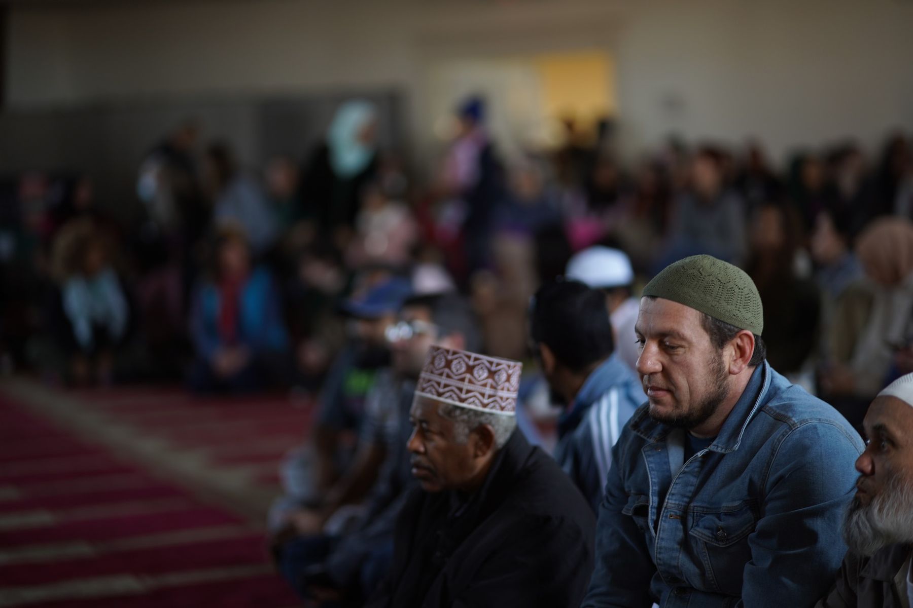 Men of different ages and backgrounds seated in the prayer hall, listening