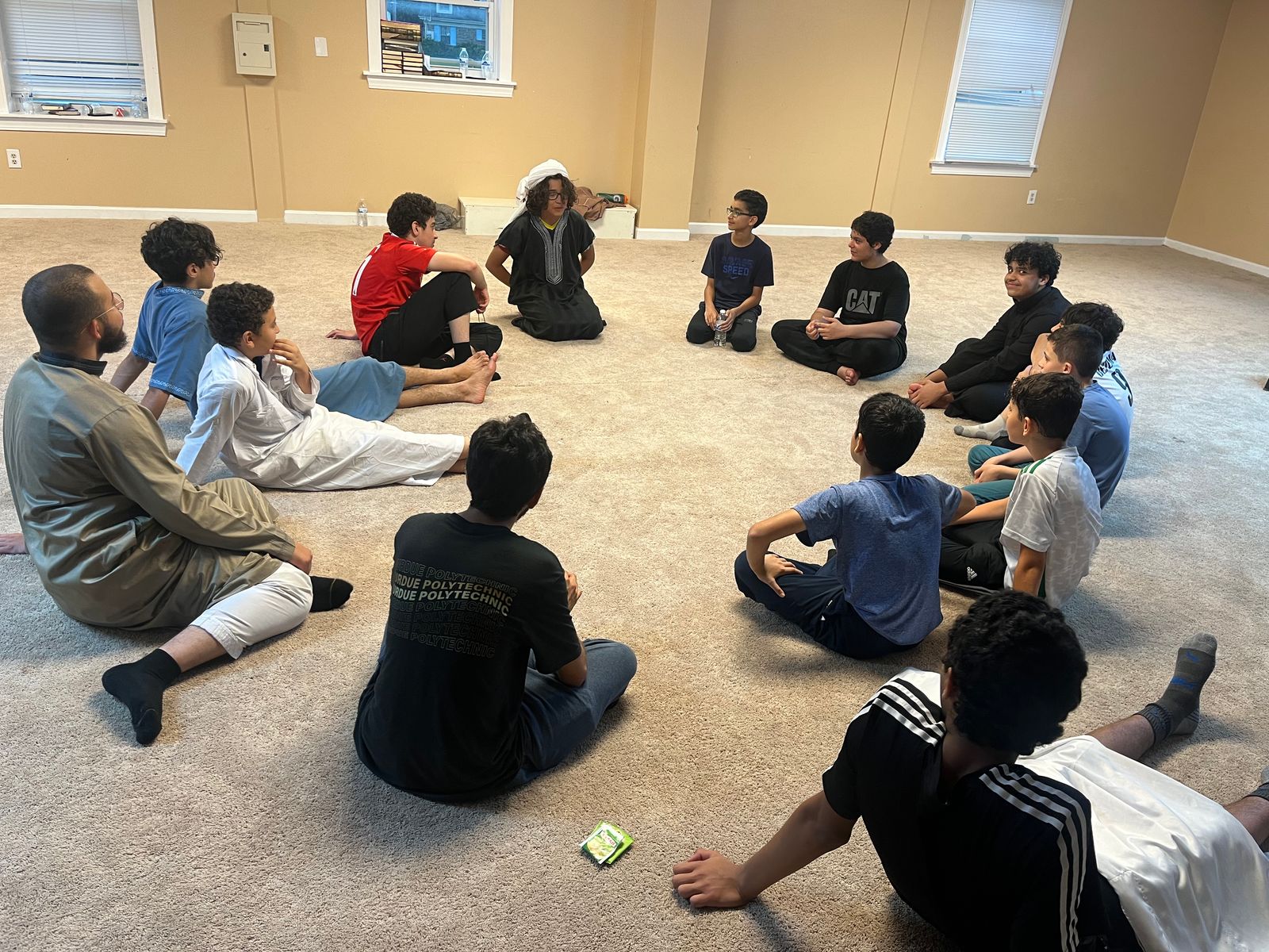Boys from Taqwa Tribe sitting in a circle on the carpet with a youth leader